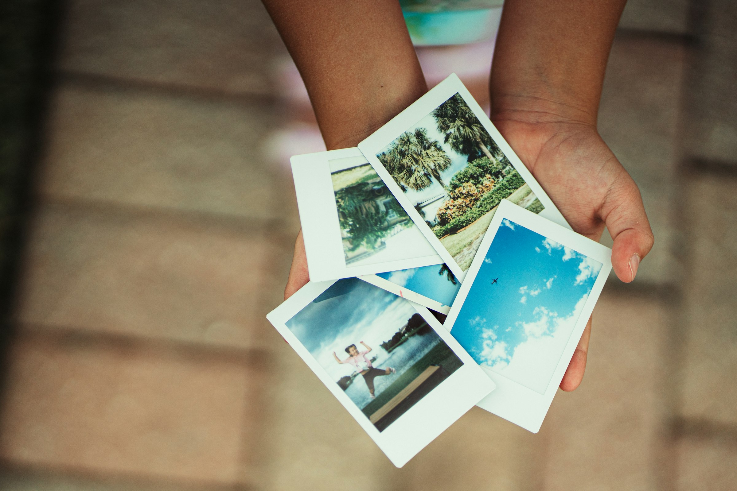 Dłonie trzymają cztery wydrukowane zdjęcia polaroid z letnimi motywami